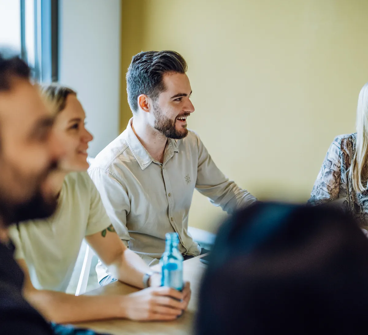 Group of people sitting at a table, smiling and holding drinks, in a casual meeting setting.