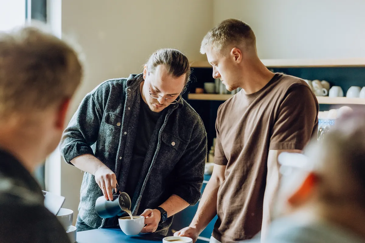 Two men in a kitchen, one pouring coffee into a cup while the other watches attentively.
