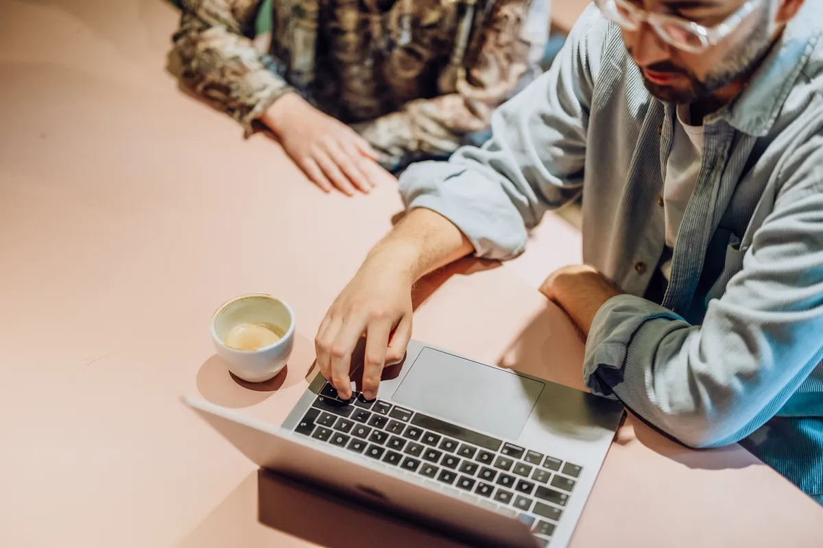 Two people sitting at a table with a laptop and a cup of coffee, focusing on the screen.